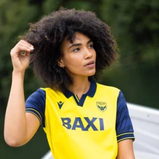 A model wearing the yellow and navy Oxford United FC 2025/26 home shirt.