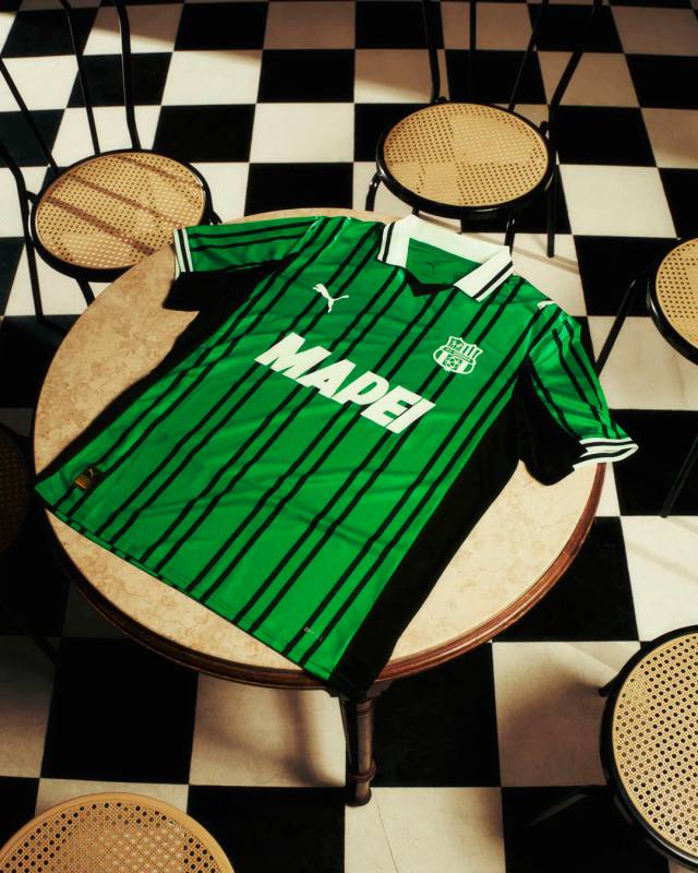 The U.S. Sassuolo 2025/26 home shirt features green and black stripes with a white polo collar, presented on a round bistro table.