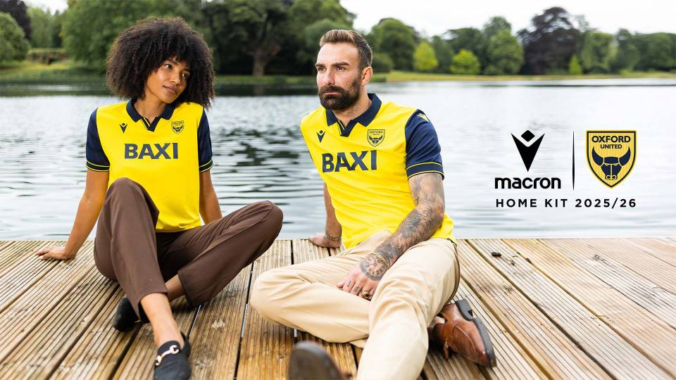Campaign photo showing two models sitting on a wooden jetty wearing the Oxford United FC 2025/26 home shirt.