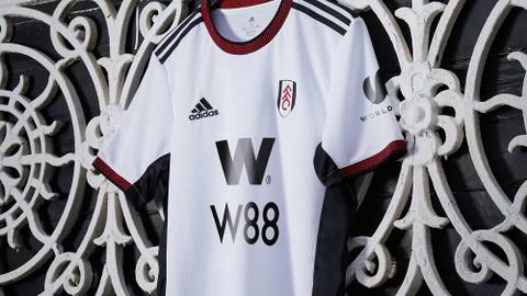 The Fulham FC 2022/23 home shirt by Adidas, featuring a white base with a red patterned collar and black detailing.