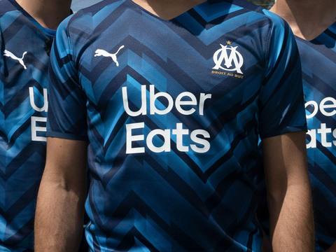 A close-up of the Olympique de Marseille 2021/22 away shirt, featuring a blue zigzag pattern, the club crest, and the Uber Eats sponsor.