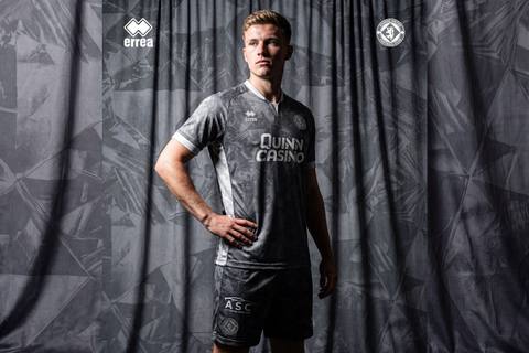 A model presents the grey Dundee United away shirt designed by Erreà, featuring a geometric pattern and white accents.
