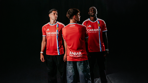 Models present the red Real Zaragoza 2026/27 away shirt, featuring a blue and white vertical stripe on the front.