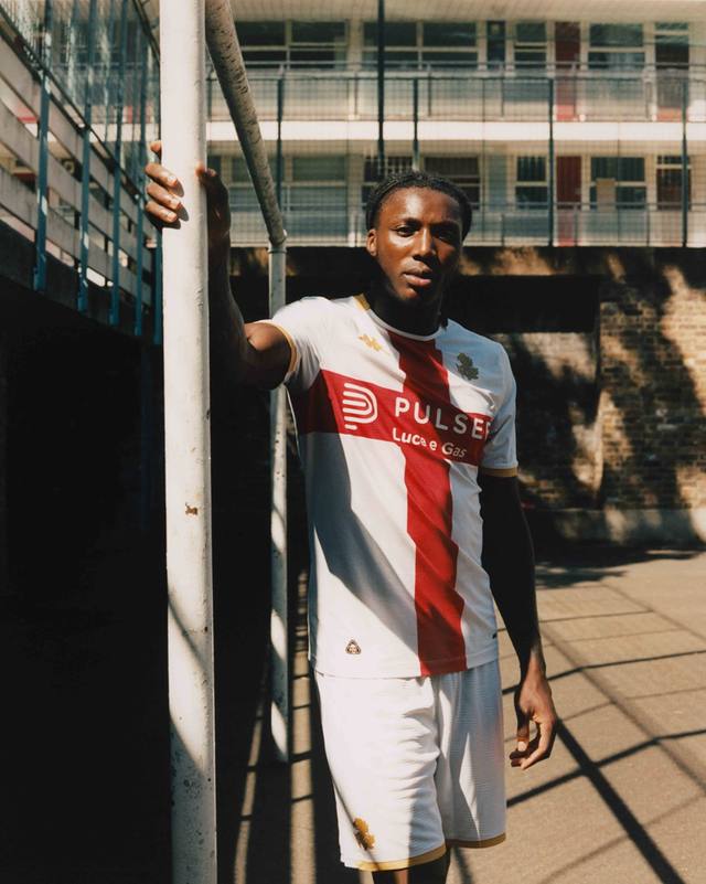 A model wearing the Genoa CFC away shirt, which features a prominent red St. George's cross on a white background.