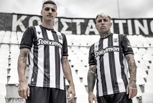 Two PAOK FC players modeling the black and white striped home shirt for the 2024/25 season in the stadium stands.