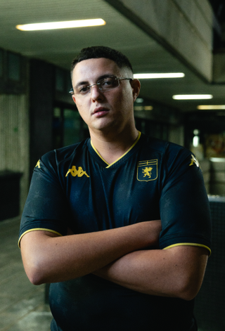 A campaign portrait of a man wearing the dark Genoa CFC third shirt with gold trim.