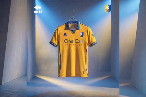 Mansfield Town home shirt by Erreà, hanging in a styled studio setting.