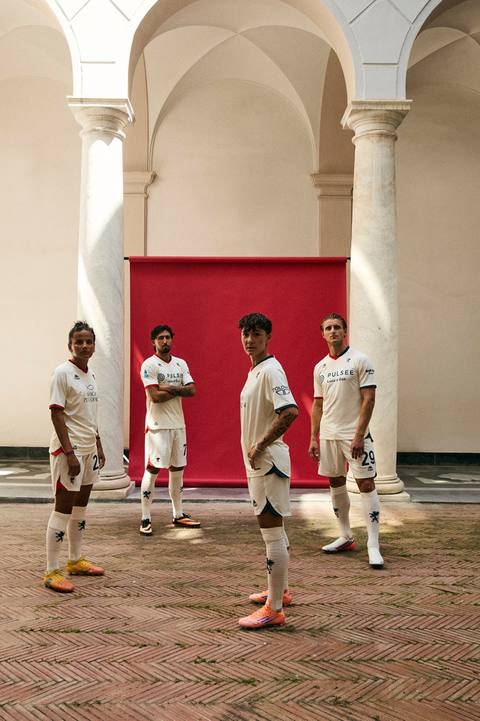 Models posing in a courtyard wearing the Genoa away kit, featuring a white base with red and blue details.