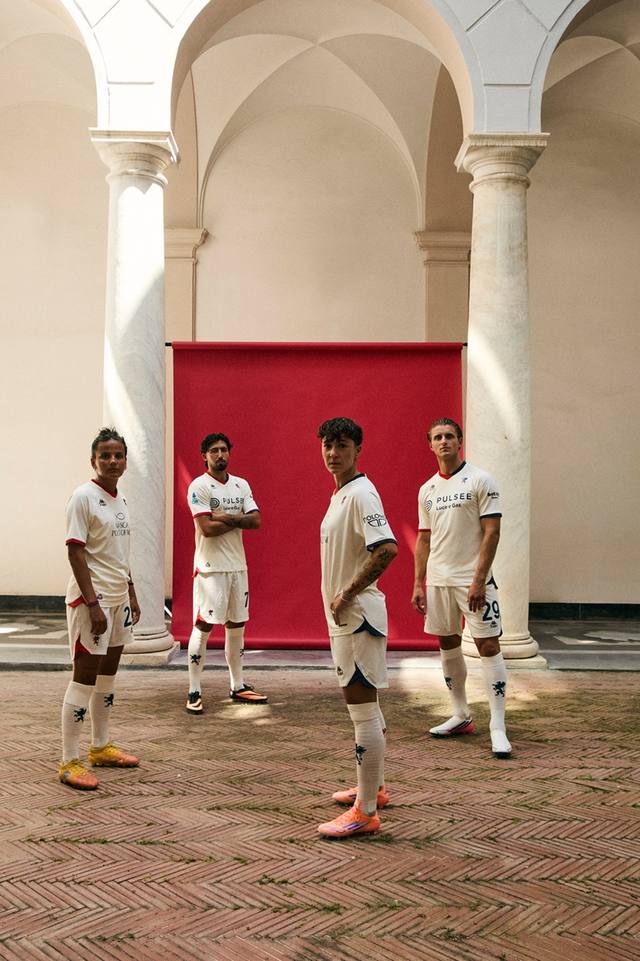 Models posing in a courtyard wearing the Genoa away kit, featuring a white base with red and blue details.