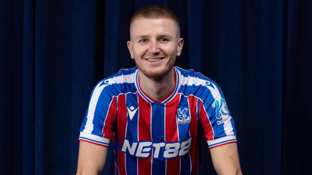 A player modeling the Crystal Palace FC home shirt with red, blue, and white vertical stripes.