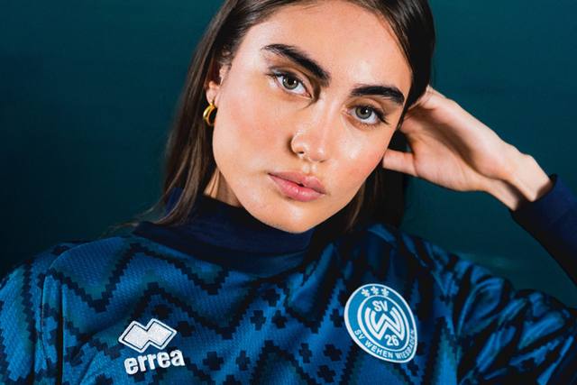 A campaign close-up of a model wearing the SV Wehen Wiesbaden third shirt by Erreà.