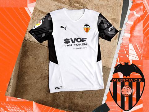 The Valencia CF 2021/22 home shirt by Puma is displayed on a textured background with orange graphics.