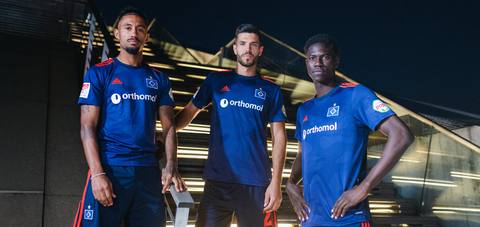 Three Hamburger SV players posing in the navy blue 2020/21 away shirt at night.