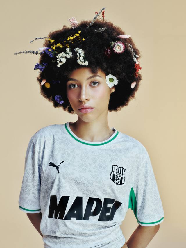 A model wears the Puma U.S. Sassuolo away shirt with a white base, subtle floral print, and green collar and sleeve trim.