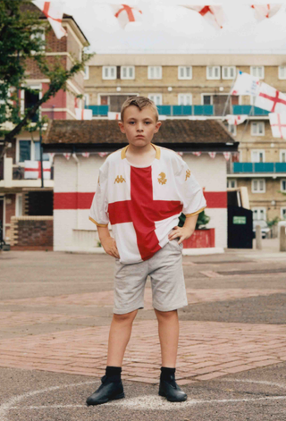 A young boy posing in the Genoa CFC away shirt featuring a red cross design.