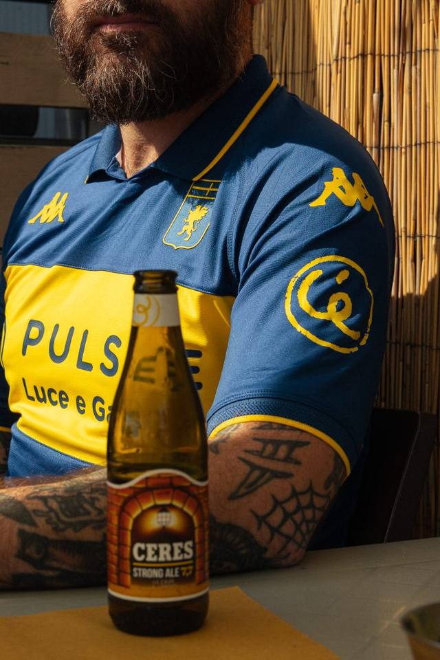 A close-up of a model wearing Genoa's blue and yellow special shirt featuring the Ceres sleeve sponsor, with a bottle of Ceres beer in the foreground.