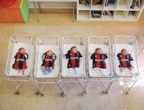 Five newborn babies dressed in Bologna FC home shirts lie in hospital cribs.