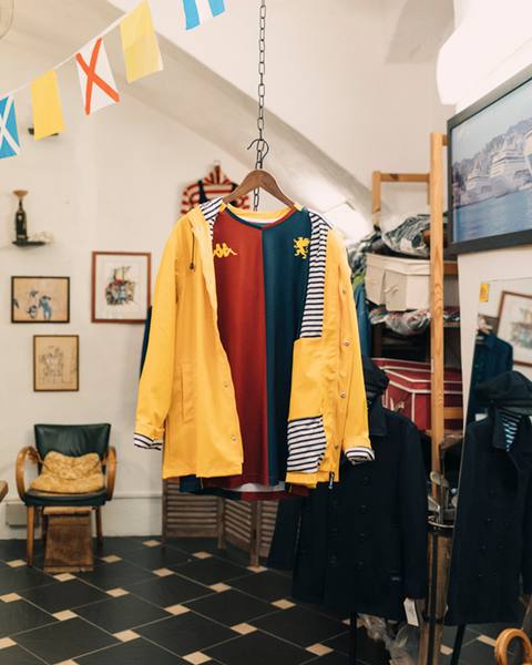 The Genoa CFC 2025/26 home shirt is shown styled under an open yellow raincoat hanging from a chain.