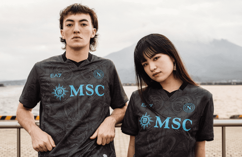 Two models posing in the SSC Napoli 2024/25 third shirt, which features a dark grey patterned base with light blue branding.
