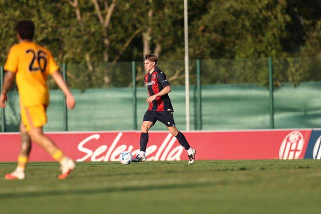 A Bologna FC player in action on the pitch wearing the 2024/25 home kit.