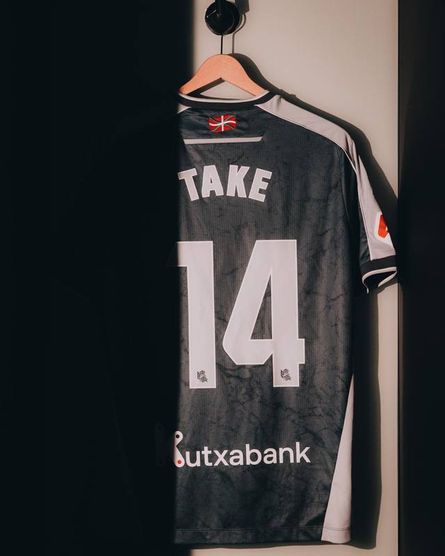 The back of the Real Sociedad away shirt on a hanger, featuring the name 'TAKE' and number 14 printed on the back.