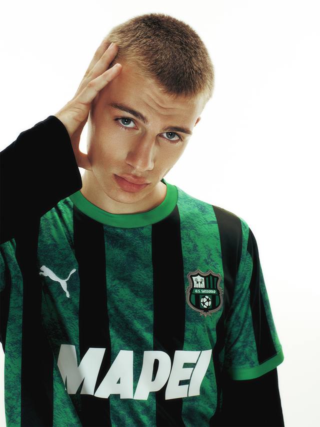 A studio portrait of a model wearing the green and black striped U.S. Sassuolo home shirt.