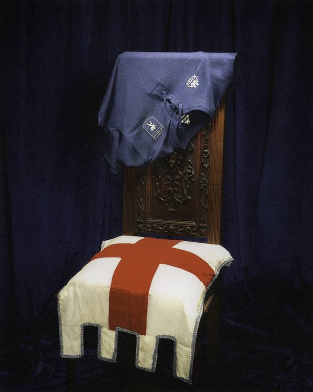 A blue Genoa third shirt with a lace-up collar is draped over an ornate wooden chair.