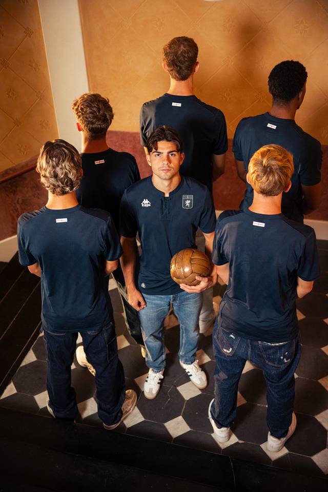 Campaign photo showing Genoa CFC's dark navy third shirt, with one player displaying the front and others showing the back design with a small St. George's Cross flag.