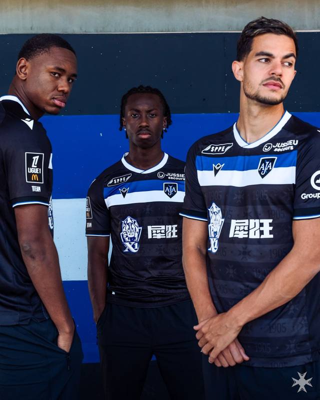 AJ Auxerre players present the new Macron away shirt, featuring a black base with a horizontal blue and white chest stripe.