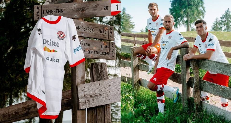 Campaign image presenting the FC Südtirol 2024/25 home shirt hanging from a wooden trail sign, alongside players posing in the full kit outdoors.
